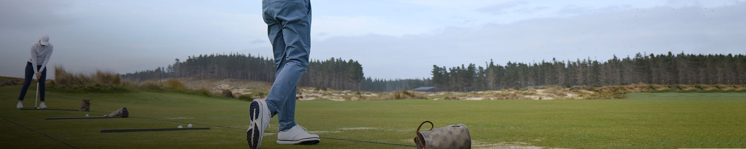 A man in KJUS Iver Pants swings at the driving range, sending grass spraying into the air.